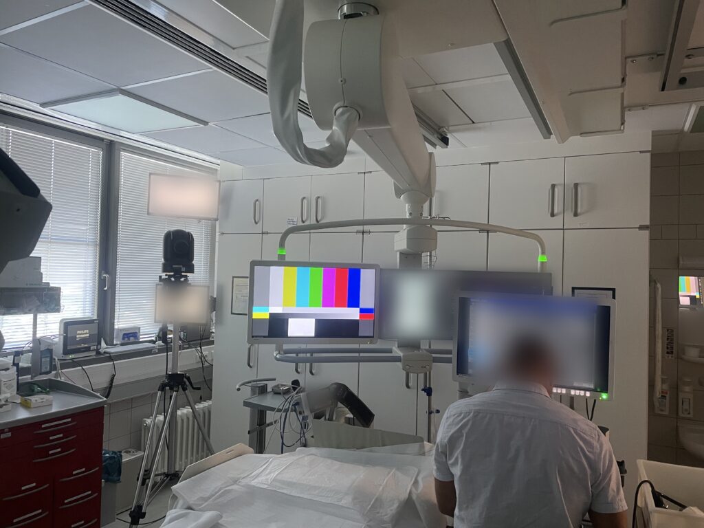 Technician setting up monitors on a ceiling-mounted boom, a PTZ camera on a tripod on the left