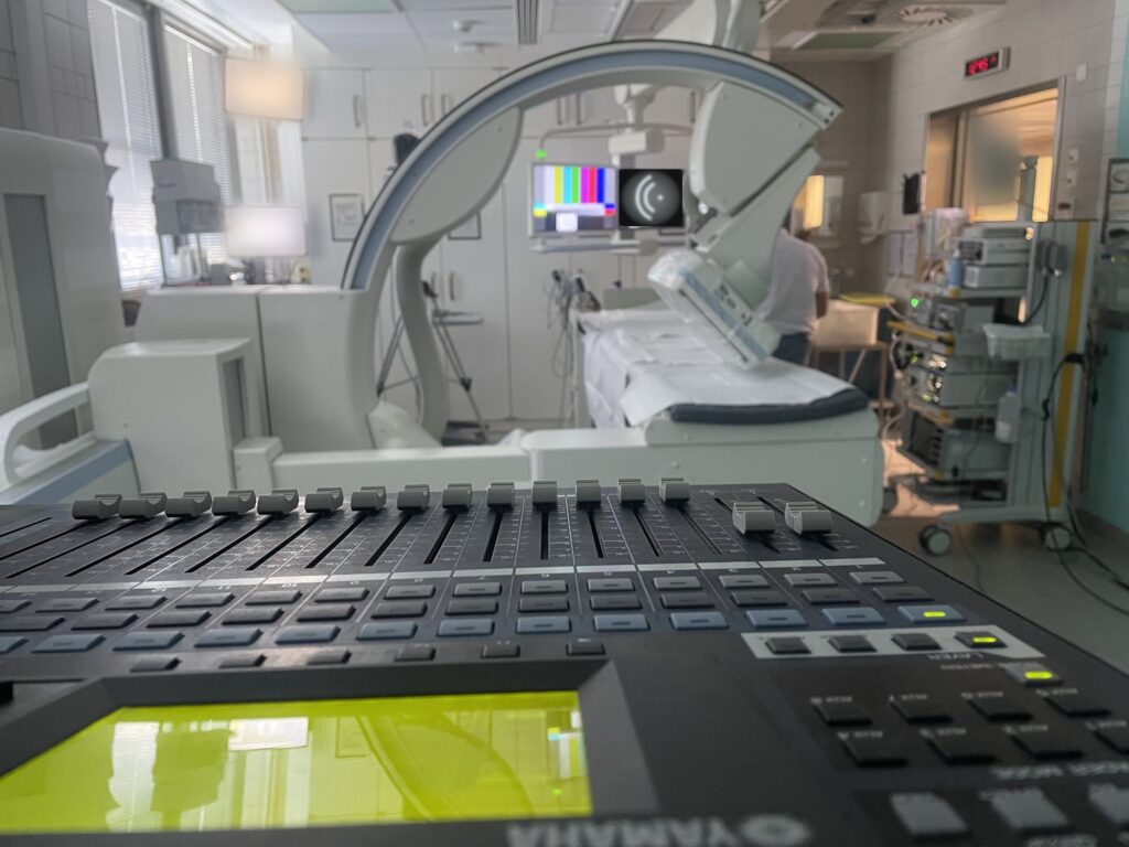 Digital mixing console with faders in the foreground, monitors with test pattern behind it